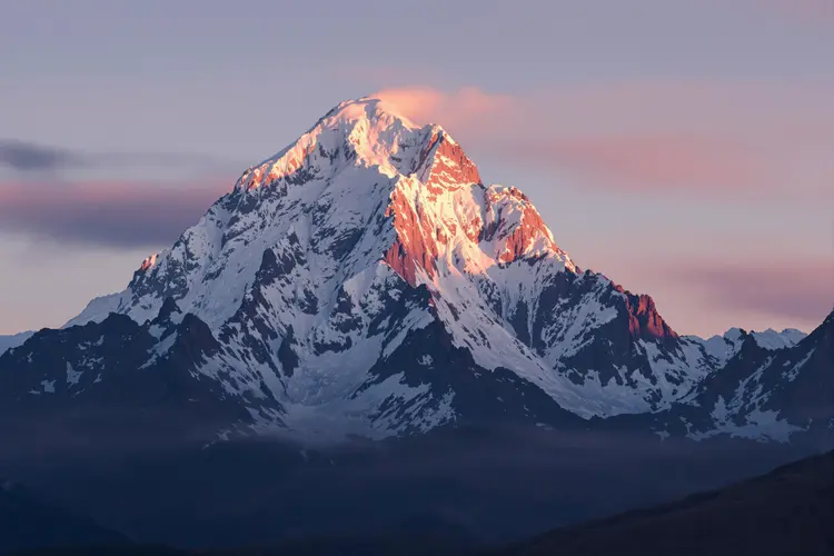 a majestic snow-capped mountain peak bathed in a warm glow of the setting sun