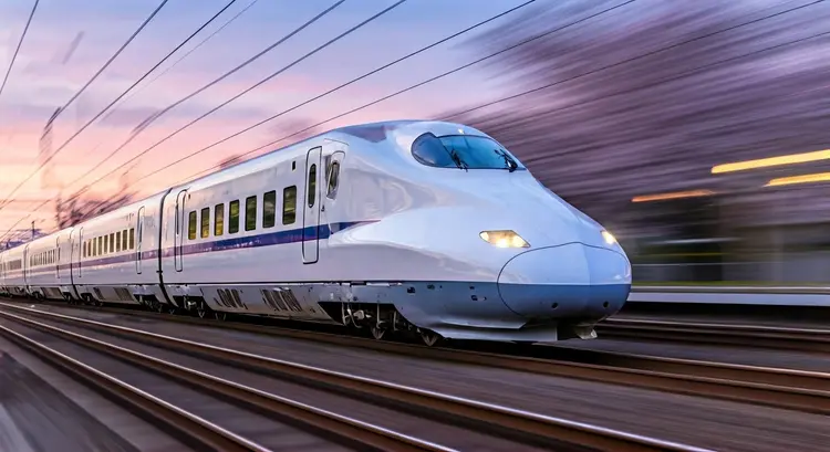 Bullet train cutting through cherry blossom petals at dusk, creating a vortex of pink and white. The polished silver exterior reflects the setting sun in a continuous streak of fire. Station lights blend into a single continuous line as the train cleaves through space. The world outside the windows is nothing but beautiful motion blur.