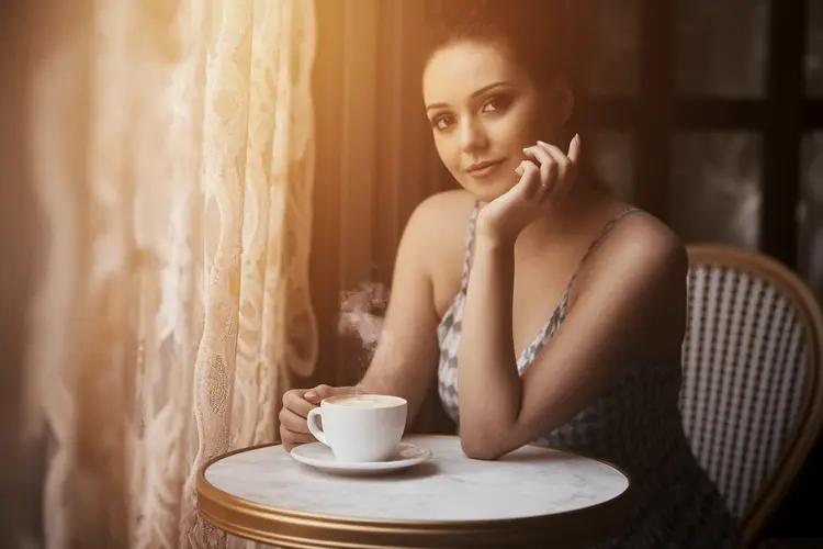A portrait photo of a woman sitting with a flat white coffee in a Parisienne cafe